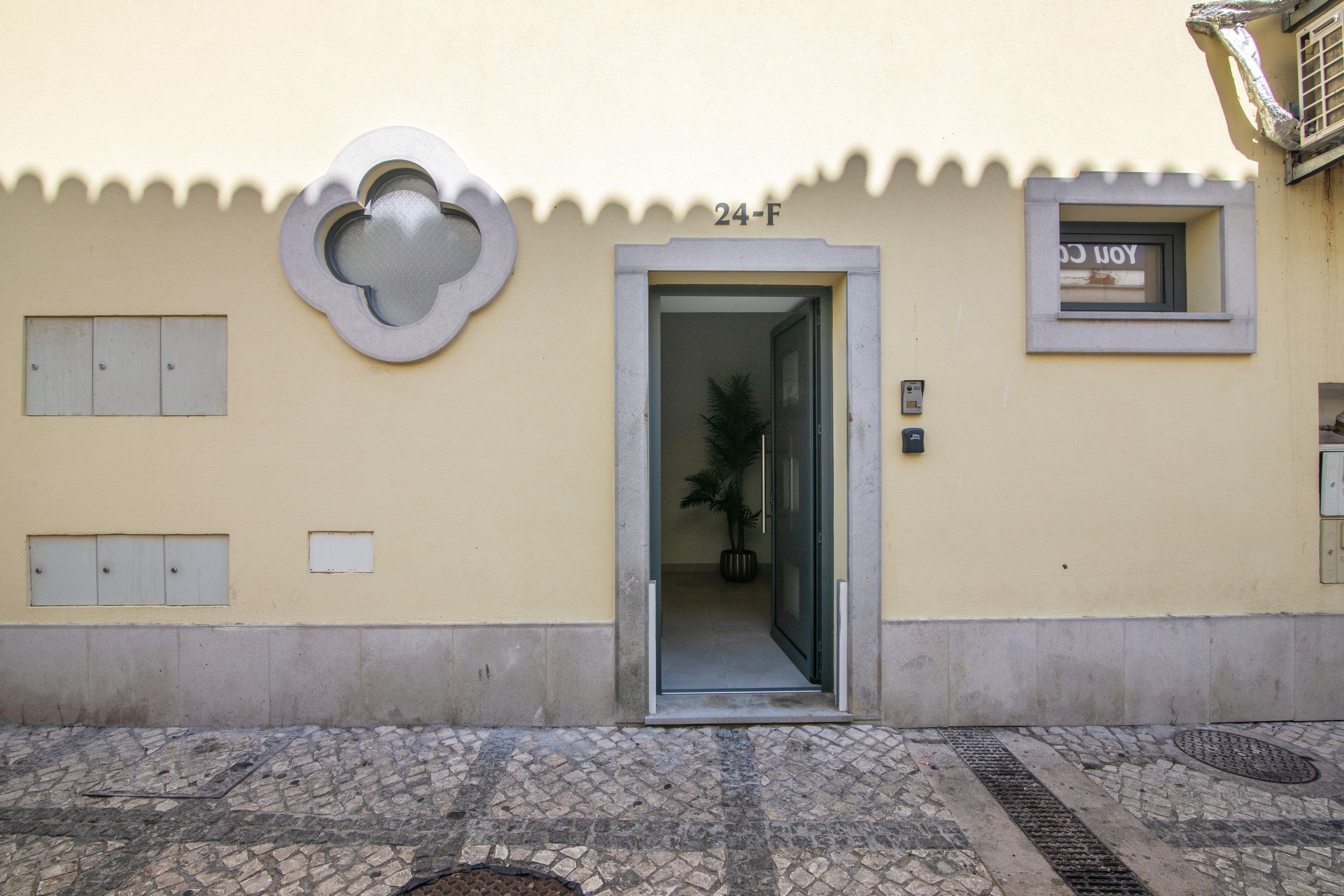 Une entrée d’immeuble avec une porte portant l’inscription « 24-F », une plante en pot à l’intérieur et une fenêtre avec une pancarte.