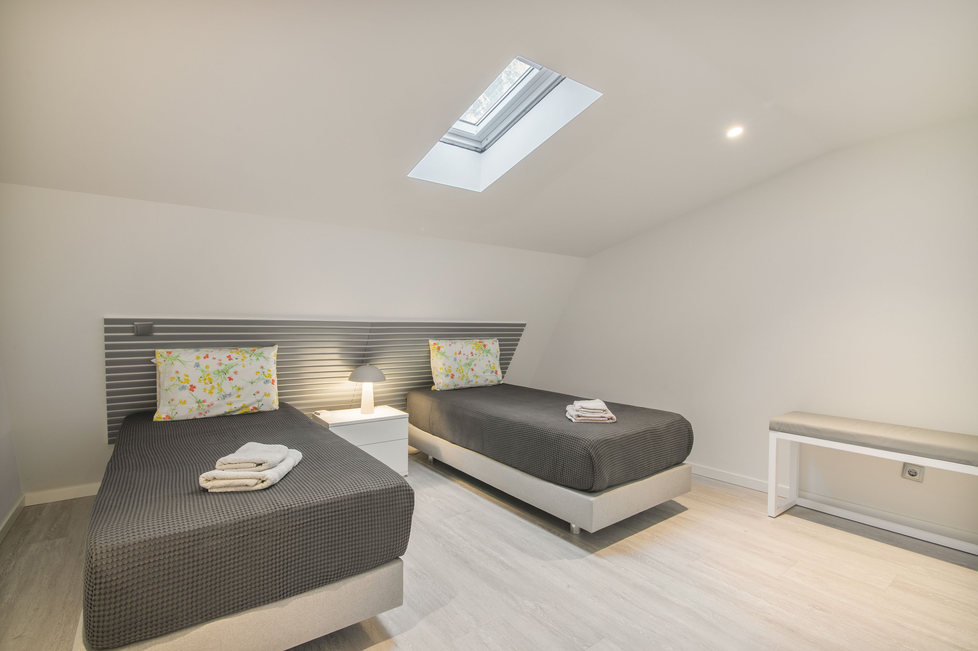 Une chambre moderne avec deux lits, une lucarne et une table de chevet avec une lampe.