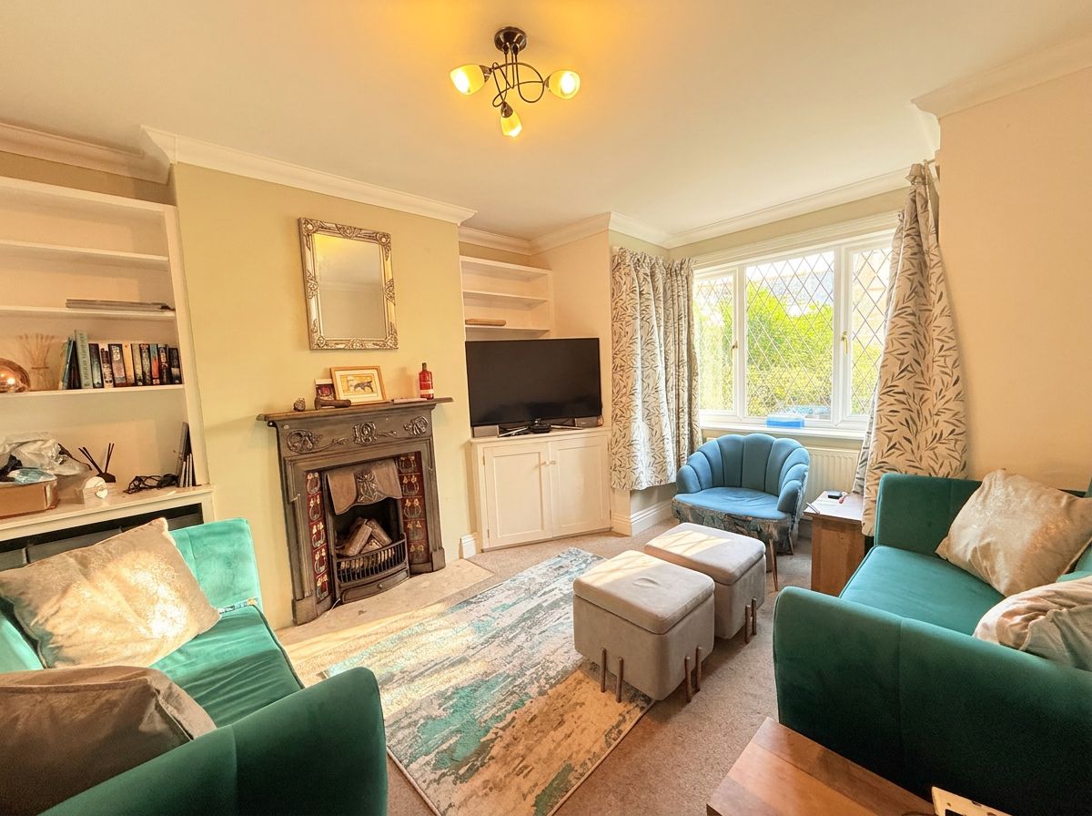 A living room with a fireplace, television, green sofas, and a large window with curtains.