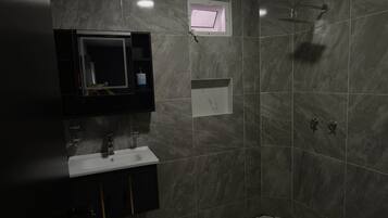 A modern bathroom with a built-in sink, a mirror, a shower, and a small window.