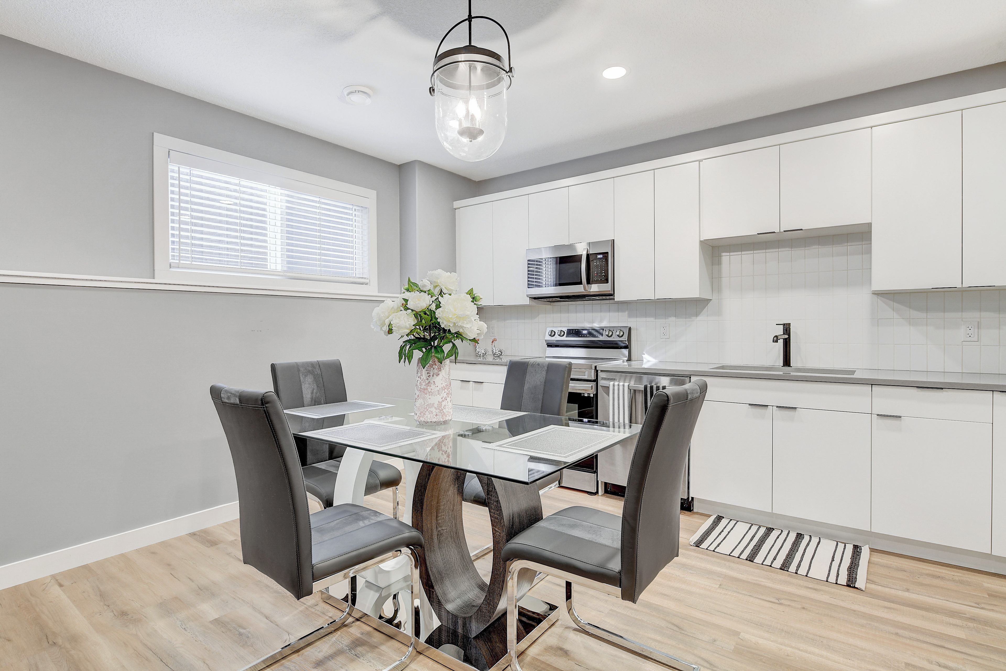 A modern kitchen with white cabinets, a glass dining table, and a hanging light fixture.