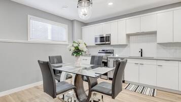 A modern kitchen with white cabinets, a glass dining table, and a hanging light fixture.