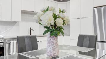 Una cucina moderna con mobili bianchi, un tavolo da pranzo in vetro con sottopiatti e un vaso con fiori bianchi.
