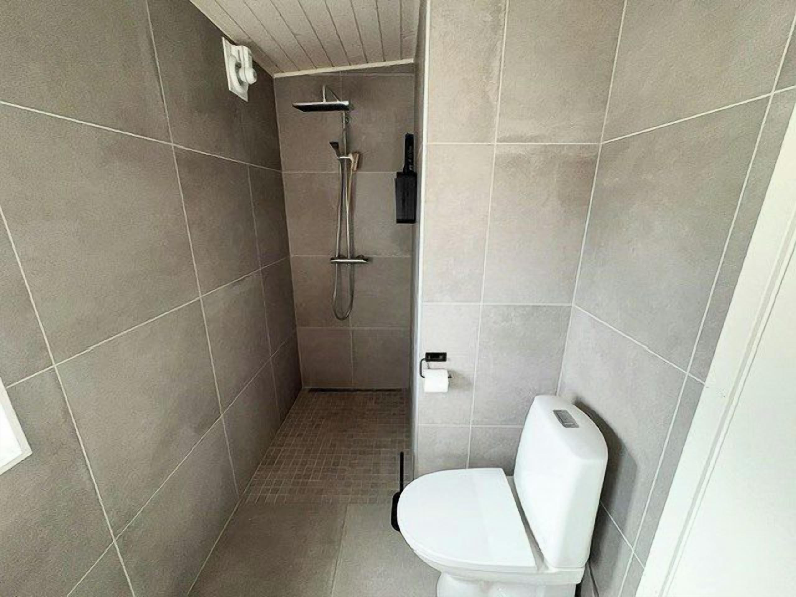 A small, enclosed bathroom with a toilet, a shower, and a towel rack.