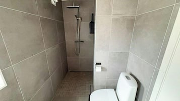 A small, enclosed bathroom with a toilet, a shower, and a towel rack.