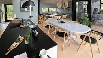 A modern kitchen with a central island, dining area with a round table, and a large window providing a view of the outdoors.