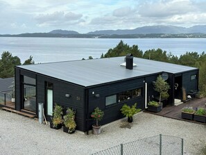 A modern black building with a flat roof, large windows, and a view of a body of water and mountains in the background. - Fjord Idyll – Peace, Nature & Views (Vestland)