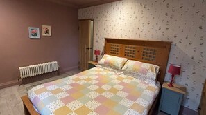 A bedroom with a wooden headboard, a quilted bedspread, two bedside lamps, a radiator, and floral wallpaper. - Cosy cottage in Wakefield. Perfect for long stays (Wrenthorpe)