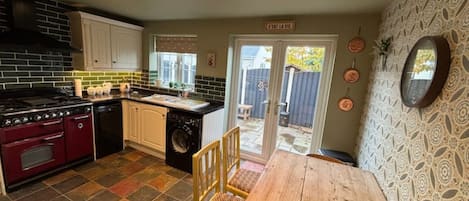 A compact kitchen with a stove, oven, and washing machine, a dining table, and a patterned wall.