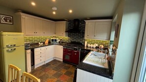 A kitchen with white cabinets, a red stove, and a green tiled backsplash. - Cosy cottage in Wakefield. Perfect for long stays (Wrenthorpe)
