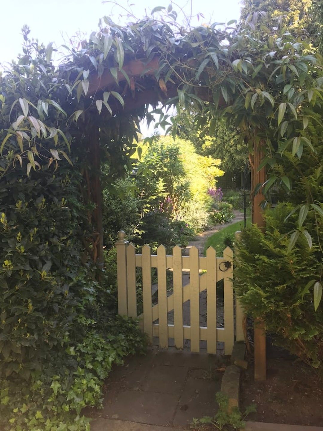 Een houten poort die uitkomt op een tuin met weelderige begroeiing en een pergola erboven.
