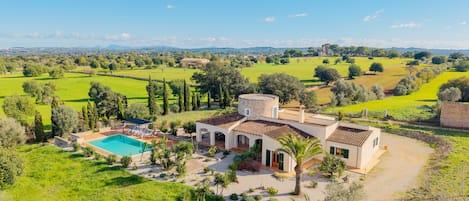 A villa with a swimming pool, surrounded by lush greenery and a view of distant hills.