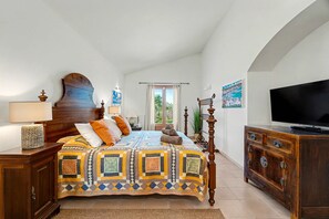 A bedroom with a large bed, a television, a wooden cabinet, and a window with curtains.