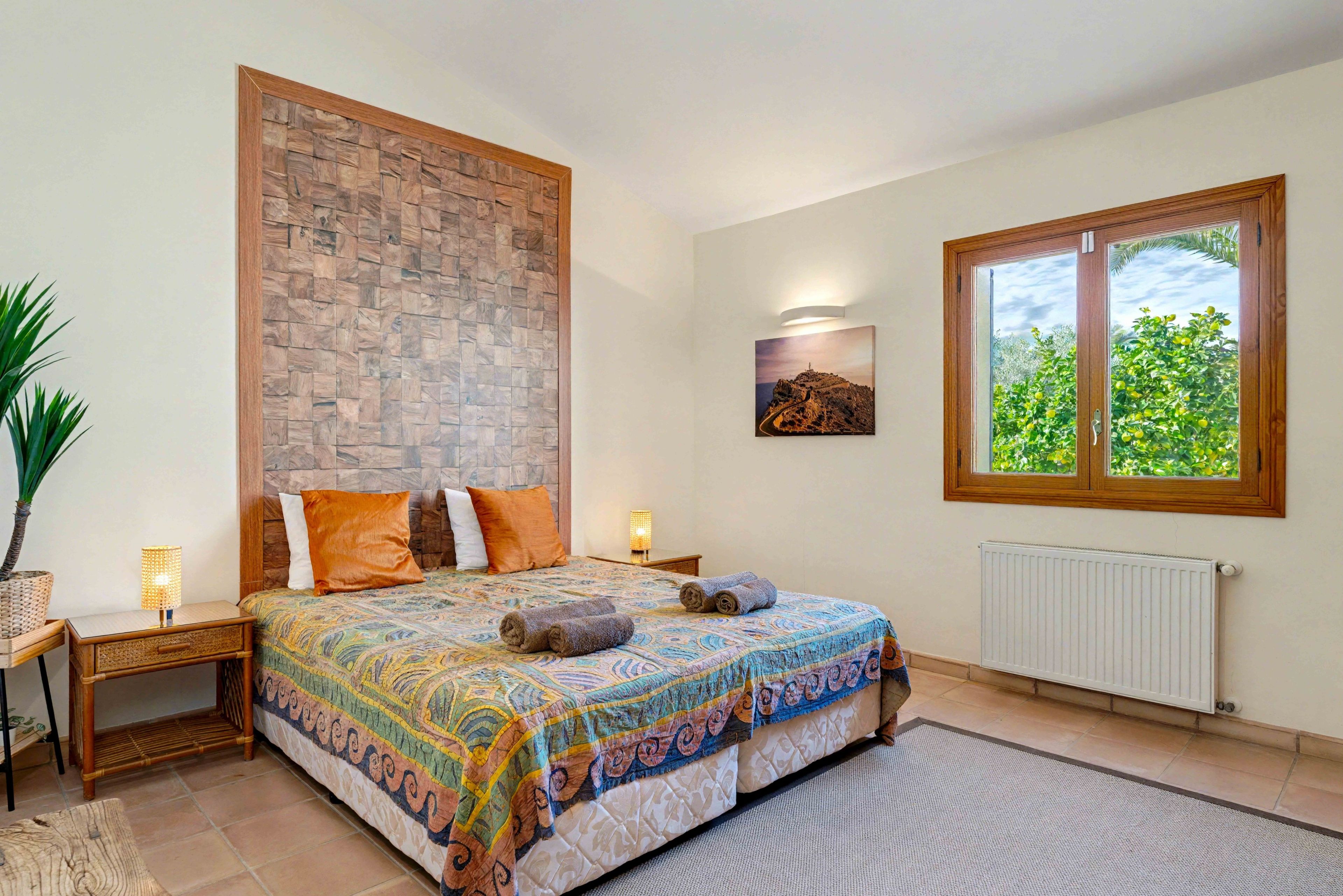 Une chambre avec un lit, un mur en pierre, une fenêtre donnant sur un beau paysage, une lampe de chevet et une petite table avec une plante.