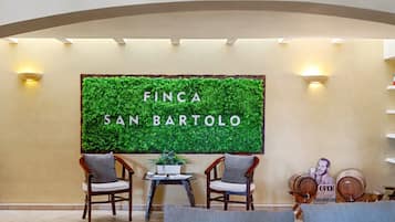 A reception area with a green wall displaying 'FINCA SAN BARTOLO' and two wooden chairs with cushions.
