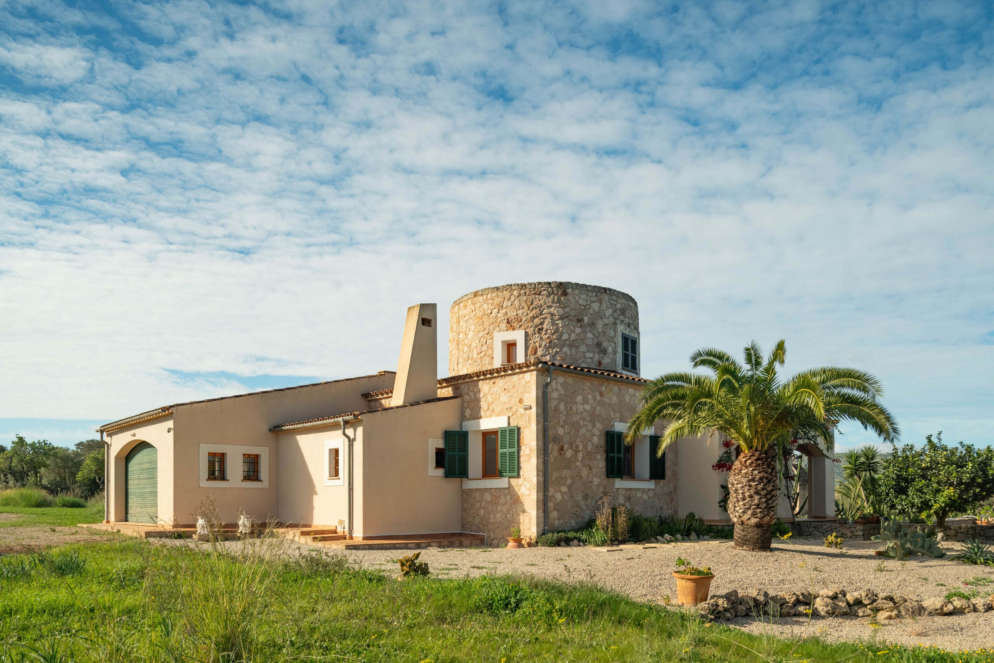 Un bâtiment traditionnel en pierre, doté d’une tour cylindrique, de fenêtres en arc de cercle et d’un palmier au premier plan.