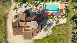 An aerial view of a resort with a swimming pool, multiple buildings, and surrounding vegetation.