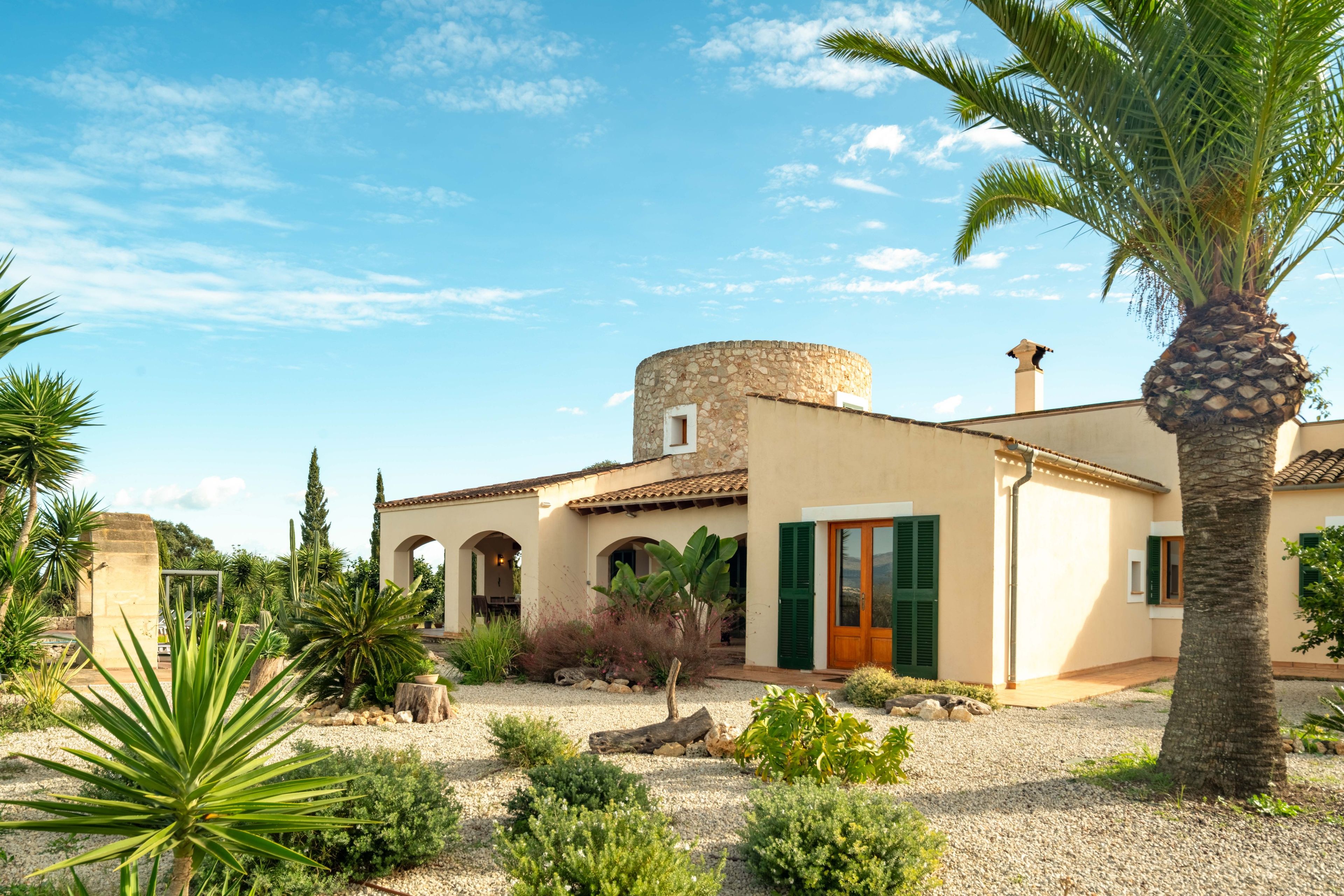 A traditional Mediterranean-style building with a stone tower, arched doorways, and a gravel courtyard.