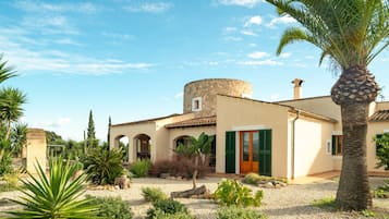 A traditional Mediterranean-style building with a stone tower, arched doorways, and a gravel courtyard.