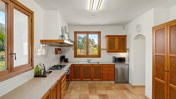 A kitchen with wooden cabinets, a stainless steel dishwasher, and a window with a view of greenery.