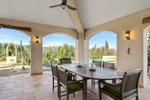 Une terrasse couverte avec une table et des chaises, un ventilateur de plafond et une vue sur un paysage montagneux.