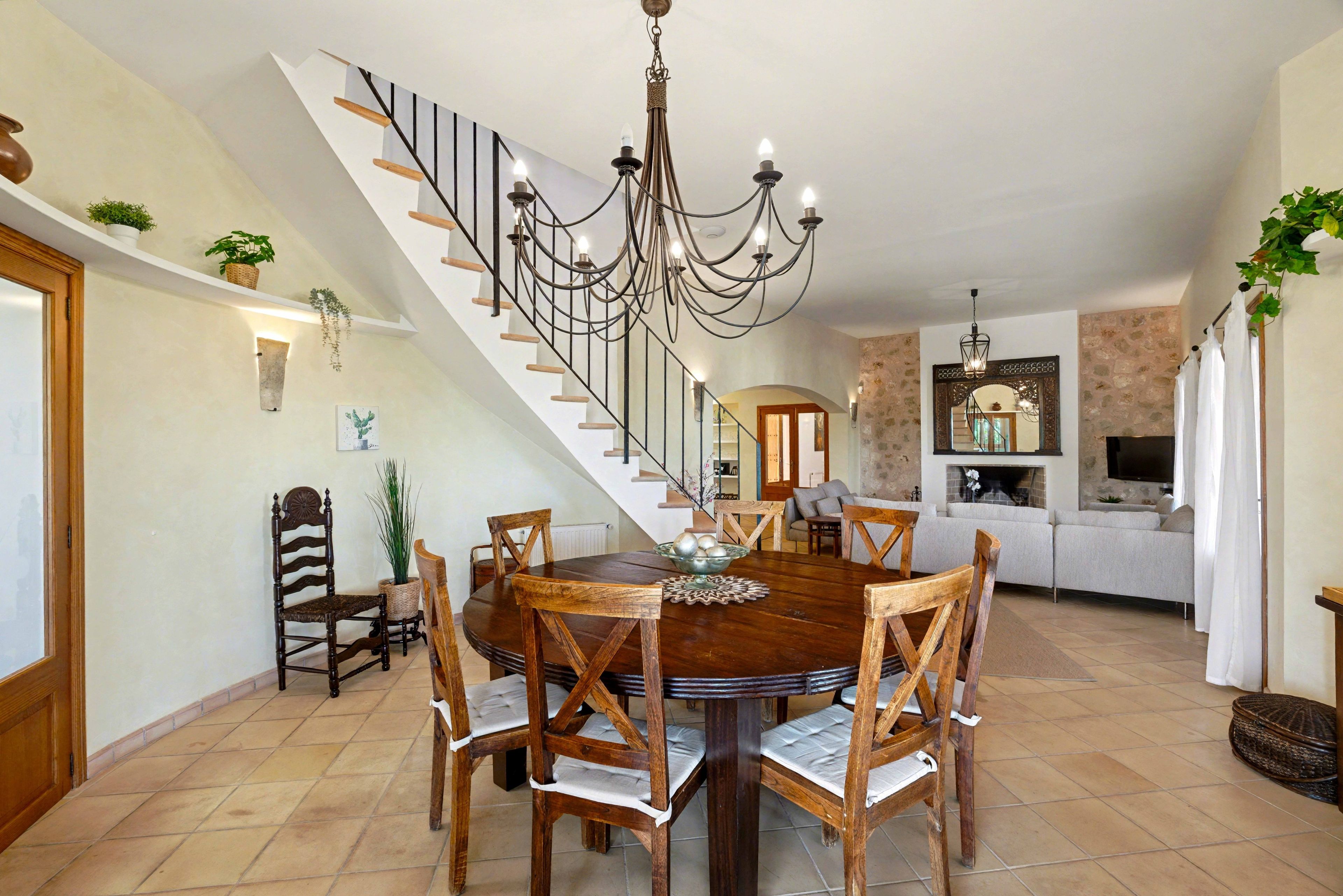 A dining area with a wooden table and chairs, a chandelier, and a staircase leading to another level.