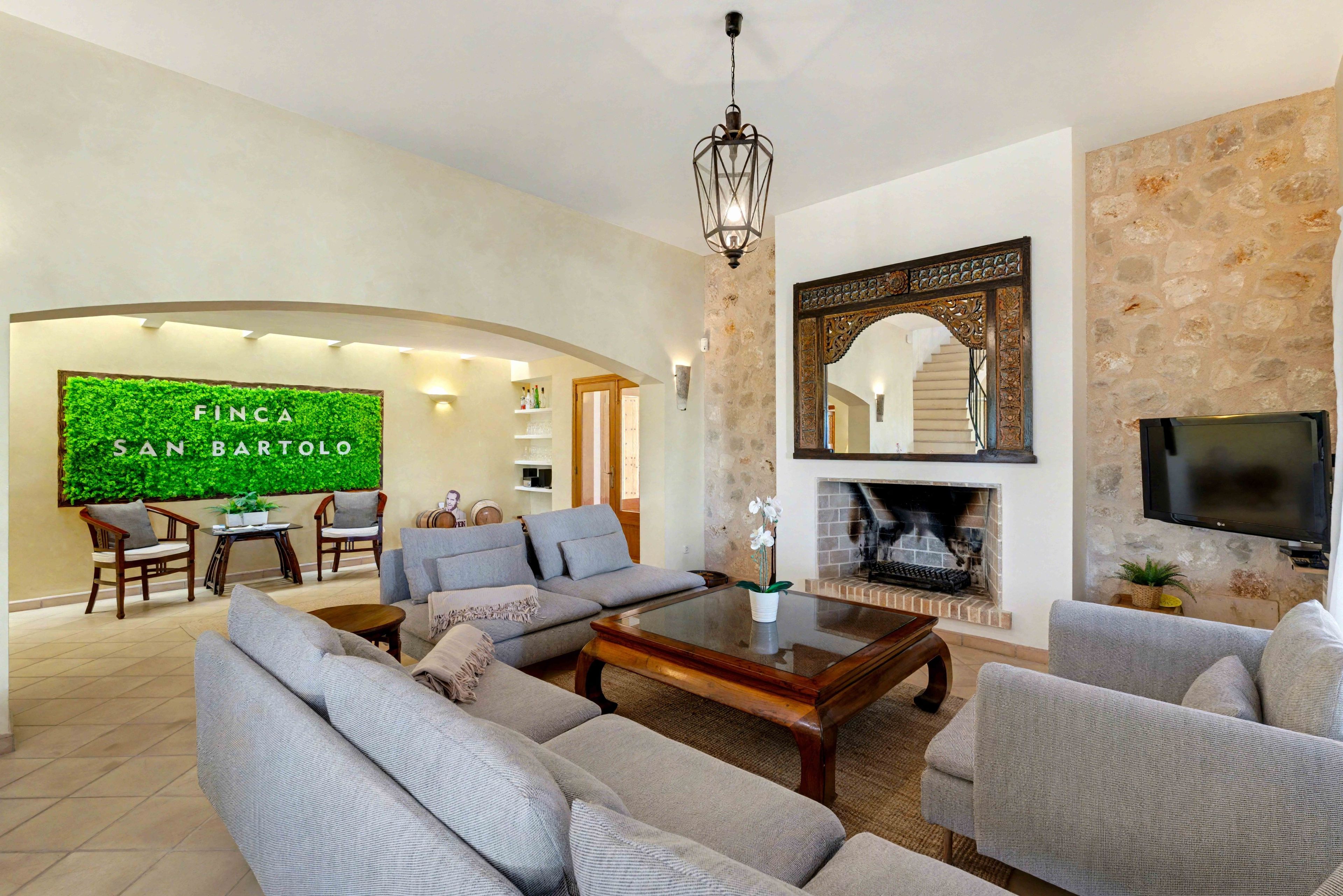 A spacious living room with a fireplace, a television, and a green wall with the text 'Finca San Bartolo'.