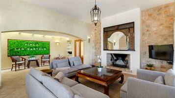 A spacious living room with a fireplace, a television, and a green wall with the text 'Finca San Bartolo'.
