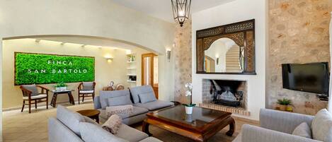 A spacious living room with a fireplace, a television, and a green wall with the text 'Finca San Bartolo'.