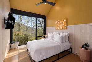 Ein Schlafzimmer mit einem Bett, einem Deckenventilator, einem Fernseher und einem gro ßen Fenster mit Blick auf Bäume.