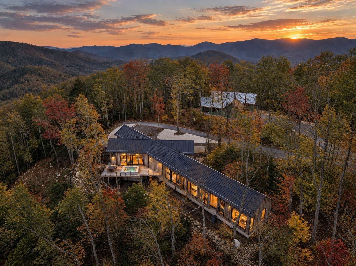 Une maison moderne dotée d’une grande terrasse et d’une piscine, entourée d’une forêt aux couleurs automnales.