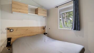 A bedroom with a wooden headboard, a bed with a grey cover, a window with curtains, and built-in shelving above the bed.