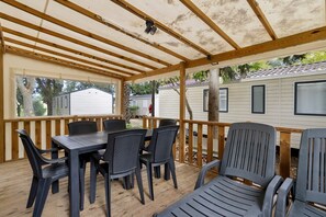 Un espacio al aire libre techado con piso de madera, sillas de plástico negro y una mesa.