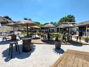 An outdoor seating area with tables, chairs, and thatched umbrellas. - Mobile home 'Bienvenue' with private terrace, Wi-Fi and air conditioning mobyl'home from 2023 (Saint-Cyprien)