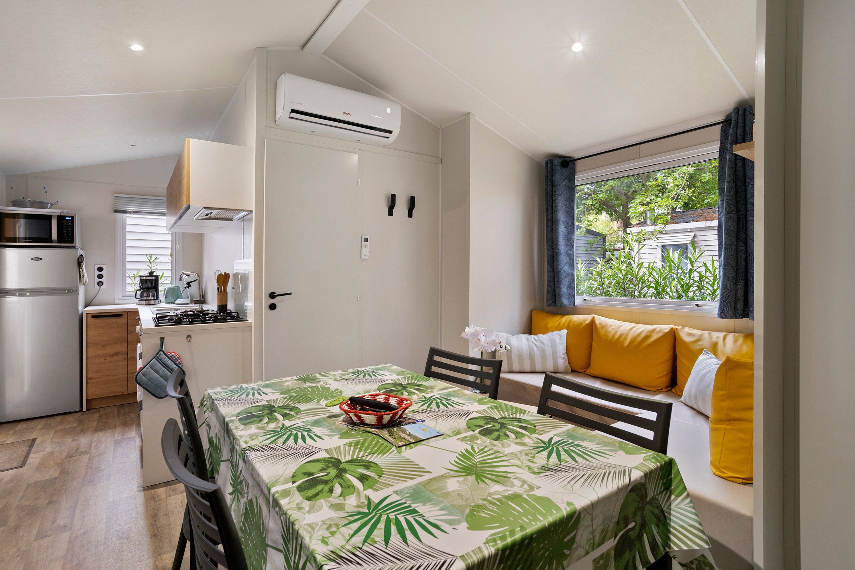 A compact kitchen with modern appliances, a dining area with a table set for two, and a window with a view of greenery.
