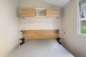 Un dormitorio con cabecera de madera, cama con colchón gris y ventana con vista a follaje.