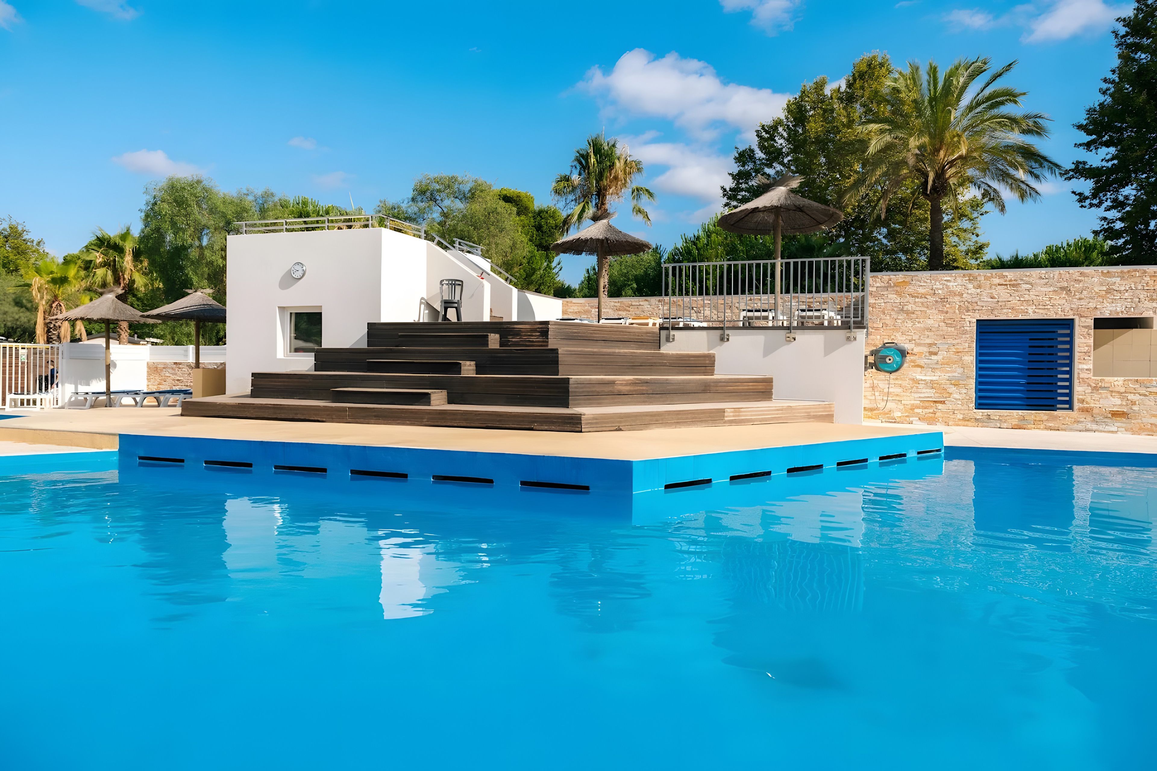 Une piscine dotée d’une terrasse ensoleillée, de murs en pierre et de palmiers.