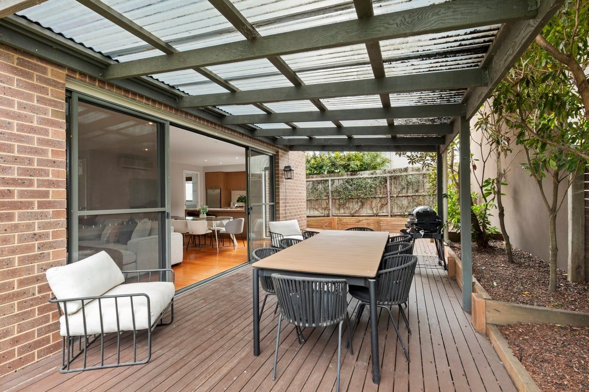 An outdoor patio with a wooden deck, metal-framed chairs, and a glass door leading to an interior space.