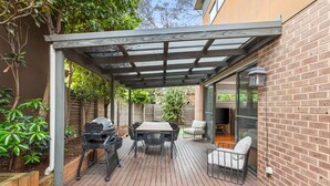 Eine überdachte Terrasse mit Grill, Tisch und Stühlen.