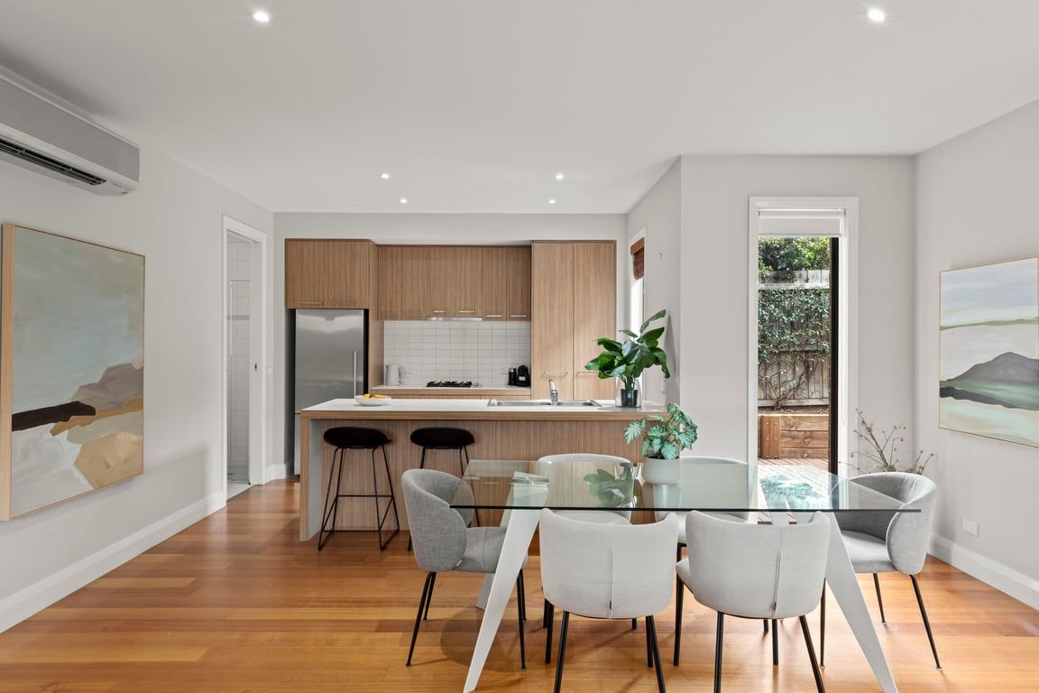 A modern kitchen with wooden cabinets, a stainless steel refrigerator, and a glass dining table with chairs.