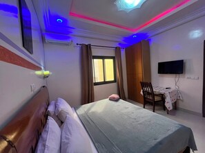 Ein Hotelzimmer mit Bett, Schreibtisch mit Stuhl, Fernseher und einem Fenster mit Vorhängen.