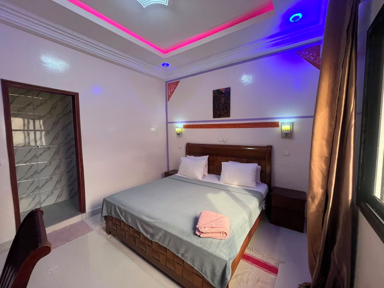 Ein Hotelzimmer mit einem Bett, Nachttischen, Vorhängen an einem Fenster und einer Tür zu einem Badezimmer.