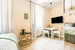 A hotel room with a bed, a desk with a chair, a TV mounted on the wall, and a window with curtains. - Rosa Taunus Apartment (Bad Camberg)