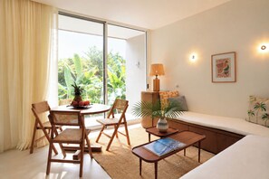 Ein modernes Wohnzimmer mit Essbereich, einer Couch, einem Couchtisch und Blick auf üppiges Grün draußen.