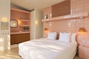 Ein Schlafzimmer mit einem Bett, Nachttischlampen, einem Spiegel und Blick ins Badezimmer.