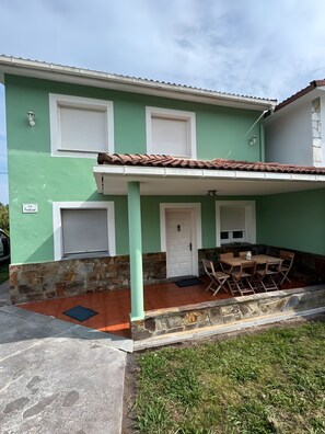 Un edificio de dos pisos con fachada verde, contraventanas blancas y techo de tejas.