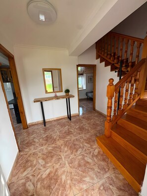 Ein geräumiger Flur mit einer Holztreppe, einem marmorierten Boden und einem kleinen Tisch mit Spiegel und Pflanze.