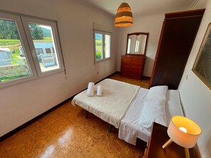 Une chambre à coucher avec un lit, une commode, un miroir et deux fenêtres.