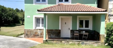 A two-story house with a tiled roof, a front porch with a table and chairs, and a small garden area.