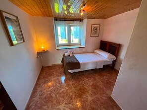 Un dormitorio pequeño y acogedor con una cama individual, una mesita de noche, una ventana con cortinas y una lámpara fijada a la pared.